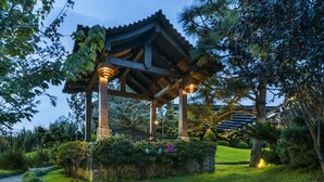 A traditional wooden pavilion with a tiled roof, surrounded by well-maintained greenery and a stone pathway.