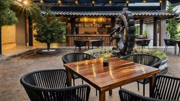 An outdoor dining area with a wooden table and black wicker chairs, a bar with a traditional design, and a decorative sculpture.