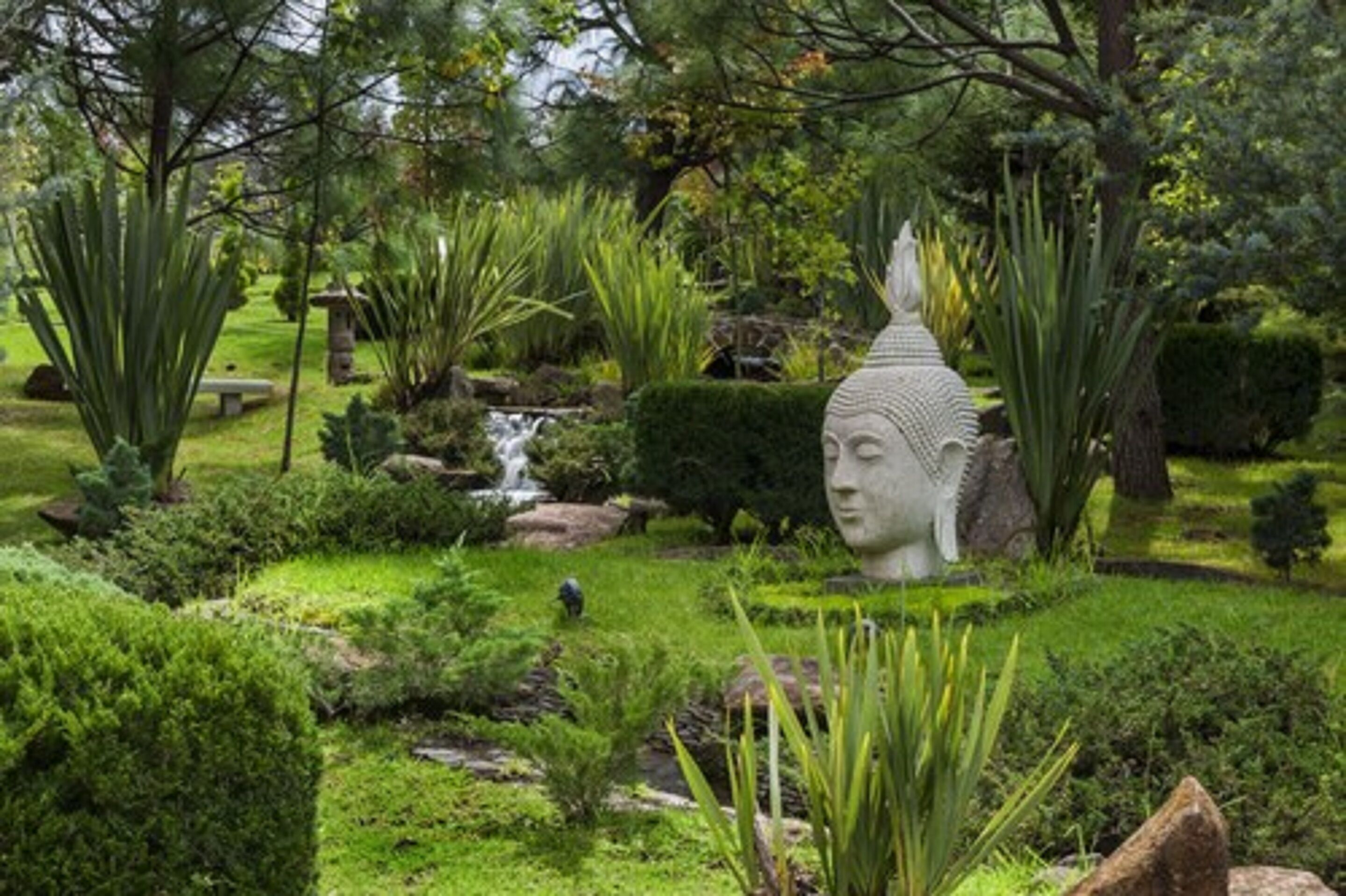 A serene garden with a statue, lush greenery, and a small waterfall.
