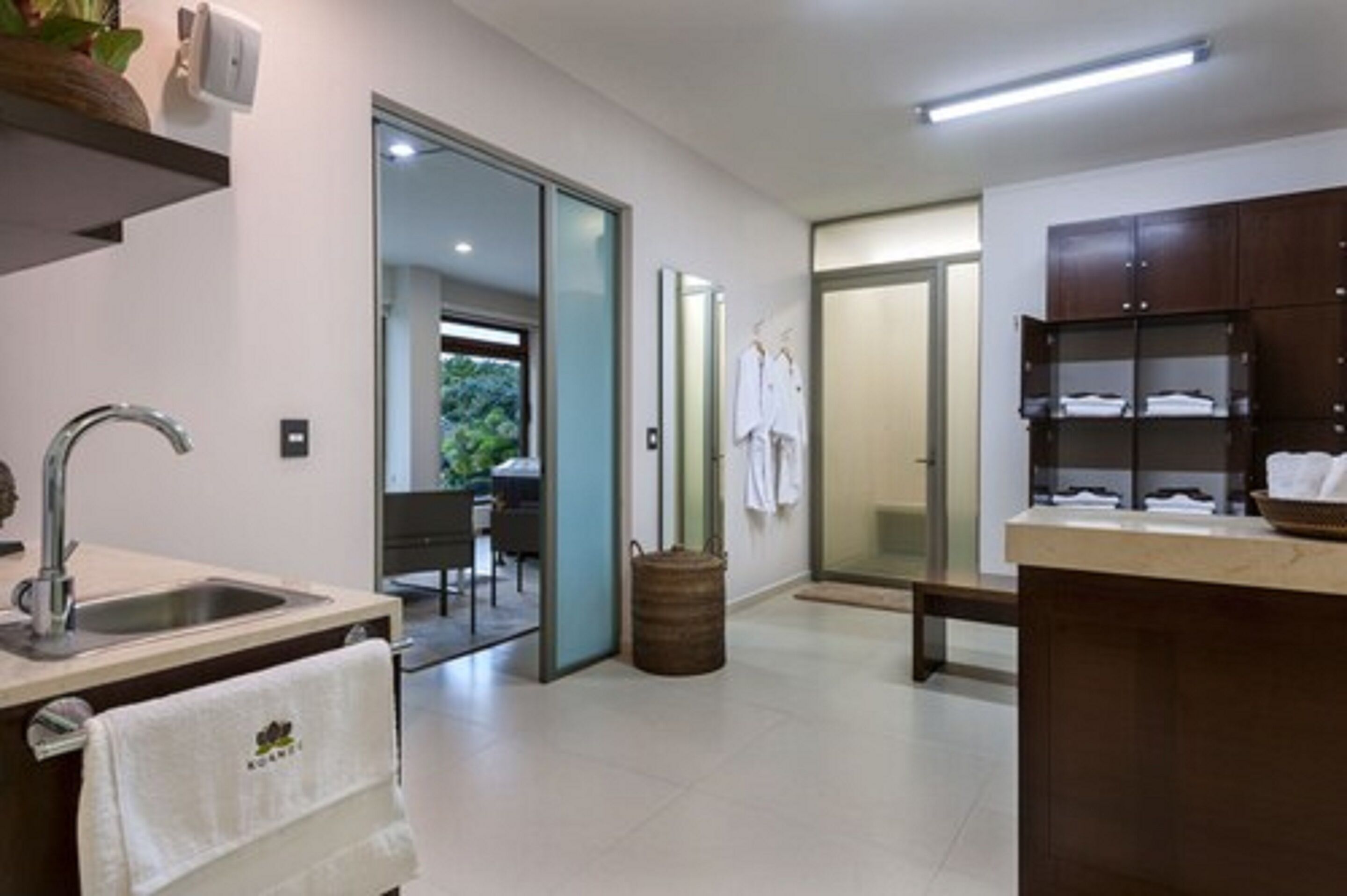 A modern bathroom with a sink, mirror, and towel rack. There is a wooden bench and a basket near the entrance.