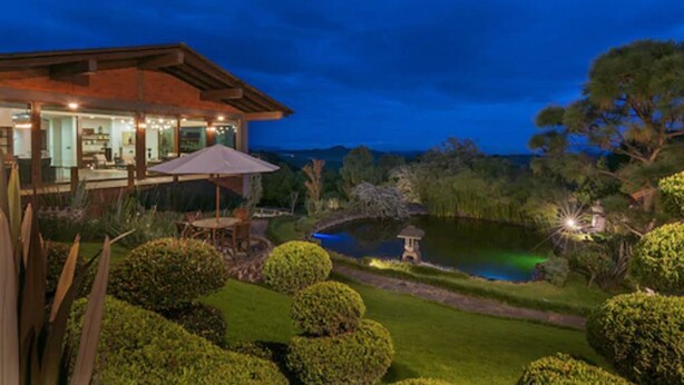 A modern house with a large deck, a pond, and well-maintained gardens.