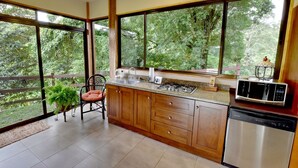 Eine Küche mit Holzausstattung, einem Edelstahl-Geschirrspüler, einer Mikrowelle und einem Spülbecken. Ein Stuhl und ein Blumentopf befinden sich in der Nähe des Fensters.