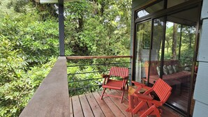Ein Balkon mit Holzdeck, zwei rote Stühle und eine Glastür zu einem Raum mit einem roten Sofa.