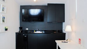 A compact kitchen with a flat-screen TV, dark cabinets, a sink, and a small table with a lamp. - Estudio con cocina, WiFi para trabajar remoto, cerca de la plaza de Ponce 301 (Ponce Pueblo)