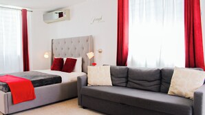 A hotel room with a bed, a sofa, red curtains, a wall-mounted air conditioner, and a wall with the text "Laugh Often". - Estudio con cocina, WiFi para trabajar remoto, cerca de la plaza de Ponce 301 (Ponce Pueblo)