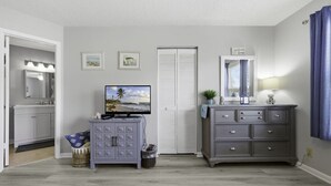 A bedroom with a TV, a dresser, a vanity, and a closet.
