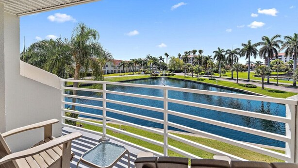 A balcony with a view of a pool, palm trees, and a building in the background.