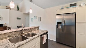 A kitchen with granite countertops, stainless steel appliances, and pendant lighting.