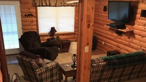 L’intérieur d’un chalet confortable, avec des murs en bois, un canapé, des fauteuils, un téléviseur et une petite table.