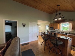 A spacious kitchen with wooden cabinets, a dining area with bar stools, a living room with a sofa, and a door leading to another room. - Private Cabin Getaway- Long Range Mountain View’s! (Marble)