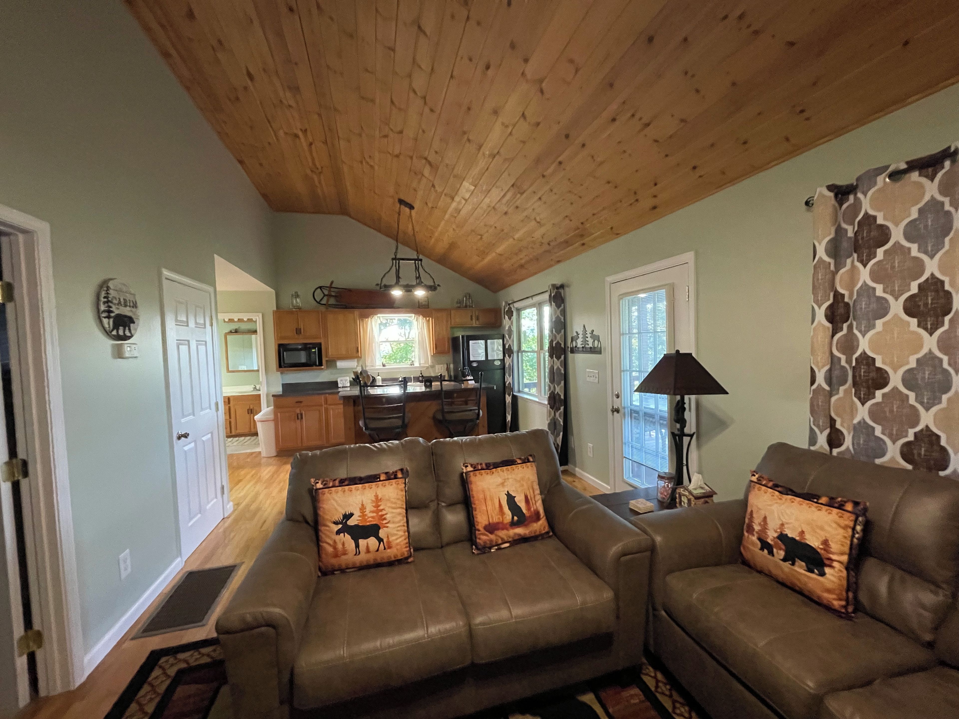A living room with a sofa set, a lamp, and a kitchen in the background.