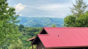 Une cabane au toit rouge, entourée de montagnes et d’arbres verdoyants.