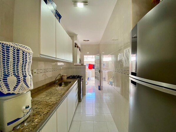 A narrow kitchen with white cabinets, a stainless steel refrigerator, and a granite countertop.