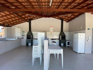 An outdoor patio with a wooden ceiling, a table with chairs, a refrigerator, and a grill.