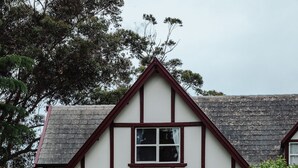 A traditional two-story house with a stone roof, surrounded by a well-maintained garden with various plants and flowers. -  Cottage by the lake (Raymond Island)