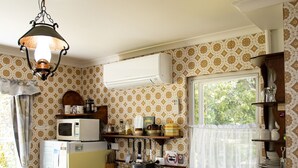 A compact kitchen with a refrigerator, microwave, and oven. There is a window with a curtain, a sink, and a hanging light fixture. -  Cottage by the lake (Raymond Island)