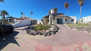 A modern house with a paved driveway, palm trees, and a clear blue sky. - Pet Friendly! Beach Bungalow, Peaceful, Private, 2 Bedroom, 2 Bath. (Puerto Penasco)