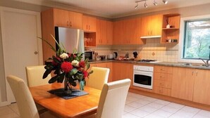 Una cuina moderna amb armaris de fusta, una taula de dinar amb caires i un ram de flors.