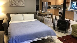 Un dormitori amb un llit gran, una zona de menjador amb taula i cadires, una cuina amb armaris de fusta, una placa de cocció i un mapa a la paret.
