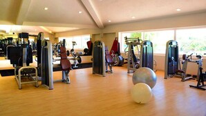 Un gimnasio con diversas máquinas de ejercicio, suelo de madera y grandes ventanales que permiten la entrada de luz natural.