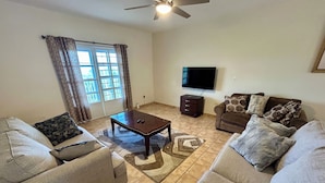 A living room with two sofas, a coffee table, a TV, and a ceiling fan. - Amazing Caribbean views! (BO Lujan,)