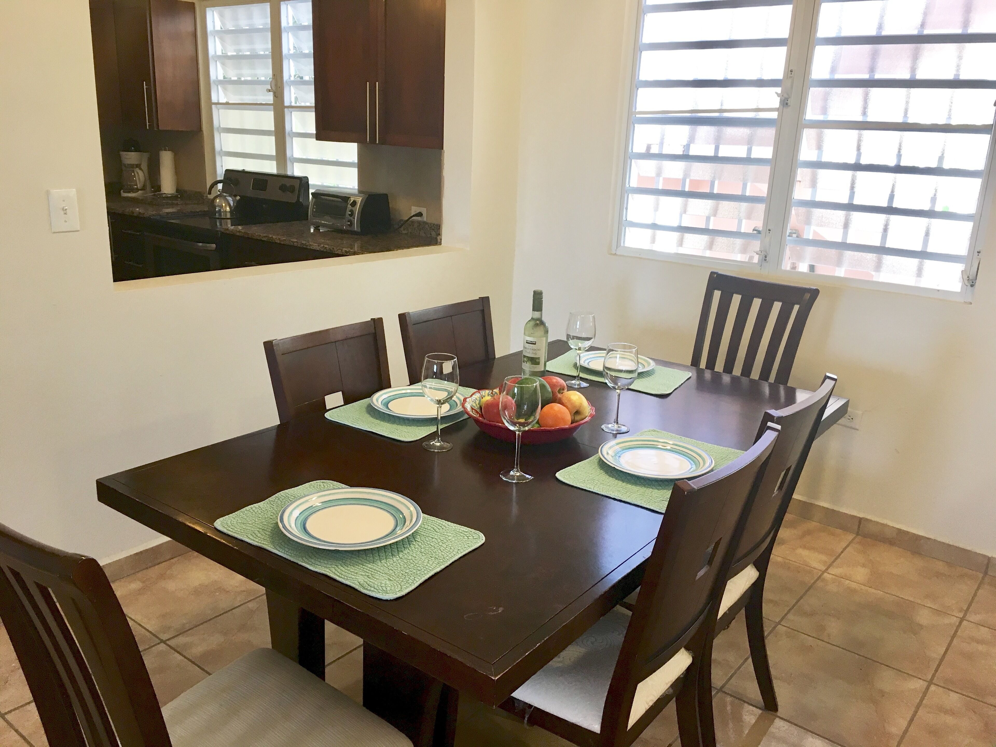 A dining area with a dark wooden table set for four, including plates, glasses, and a bowl of fruit.