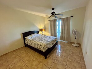 A bedroom with a bed, a ceiling fan, a standing fan, and a window with curtains. - Amazing Caribbean views! (BO Lujan,)