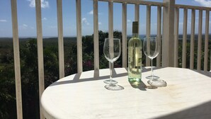 A table with a bottle of wine and two glasses on a balcony overlooking a scenic landscape. - Amazing Caribbean views! (BO Lujan,)