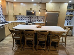 Una cocina moderna con armarios de madera, una isla central con sillas, microondas, estufa y refrigerador.