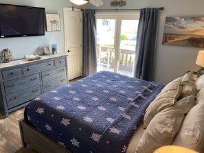 Un dormitorio con cama, cómoda, televisor y vistas al exterior.