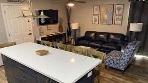 Une cuisine avec un îlot central, un coin repas avec des chaises, un canapé en cuir noir et un fauteuil à motifs.
