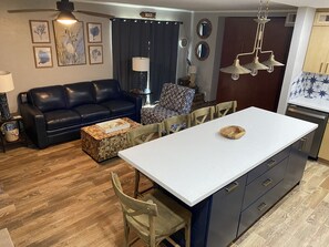 Una cocina moderna con una isla central, piso de madera y un rincón de comedor con un sofá de cuero negro y sillas estampadas.