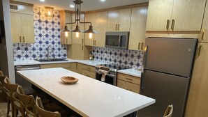 Une cuisine moderne dotée d’un îlot central, de meubles en bois, d’un réfrigérateur en acier inoxydable et d’un four à micro-ondes.