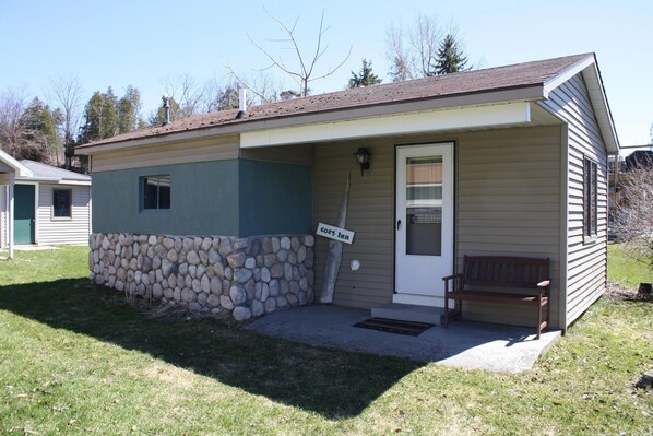 A small, single-story building with a stone foundation and a wooden bench outside.