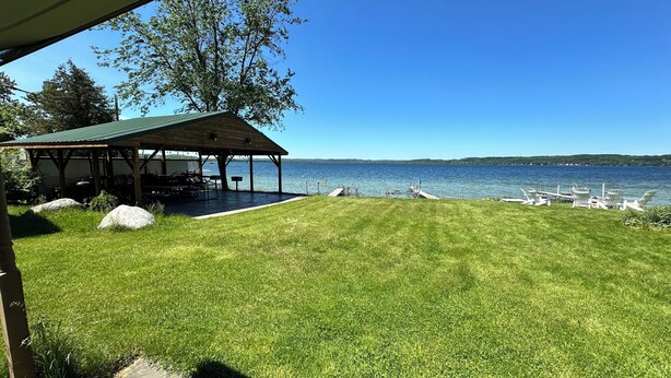 A grassy area with a covered pavilion, a dock with boats, and a clear view of the water.