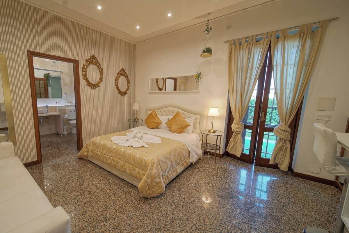 A hotel room with a bed, a sitting area, a bathroom, and a view of the outdoors.