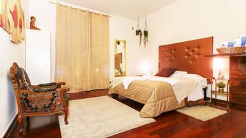 Un dormitorio con una cama de cabecera de madera, una silla decorativa, un espejo grande y una mesita de noche de madera con una lámpara.