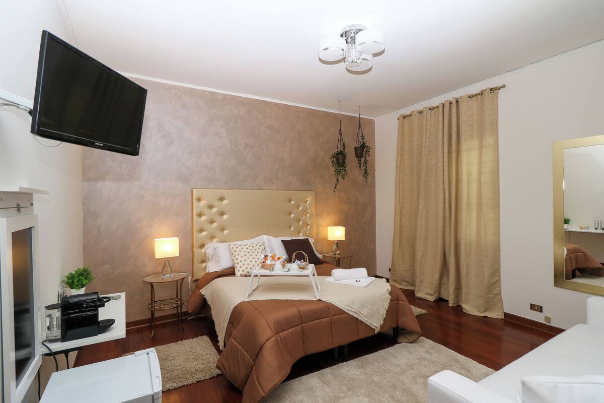 A hotel room with a large bed, bedside tables, a flat-screen TV, a ceiling fan, and a large mirror.