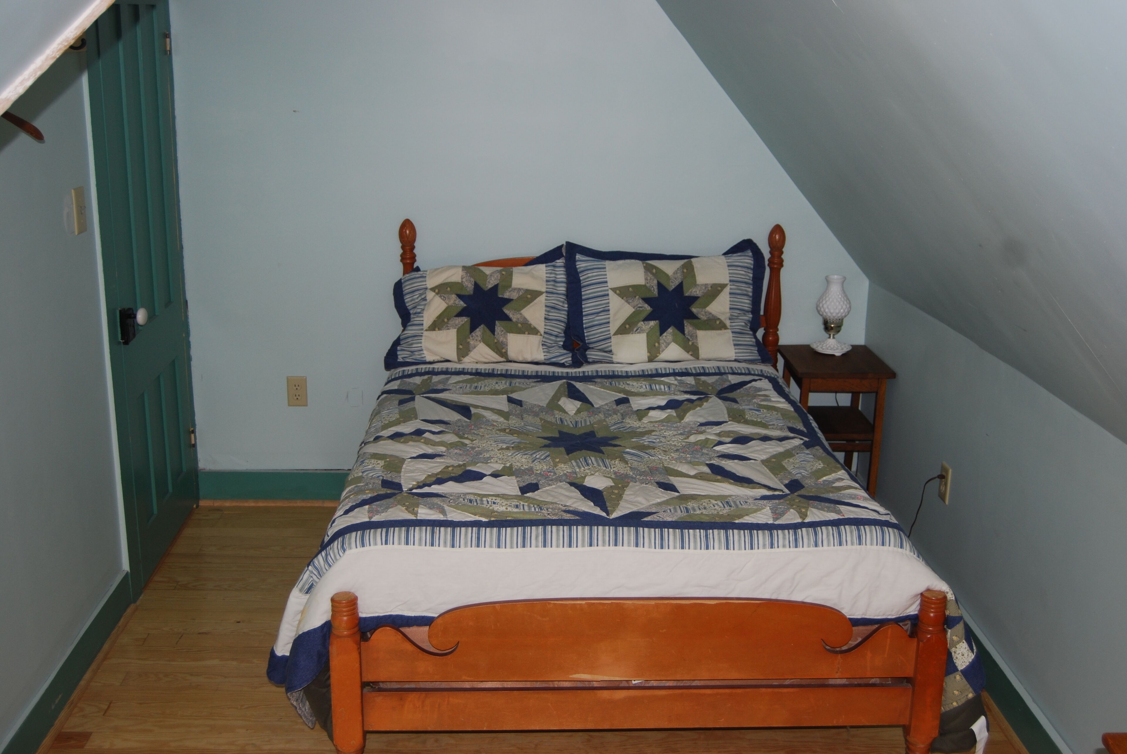 Een slaapkamer met een houten bed, een quilt en een klein nachtkastje met een lamp.