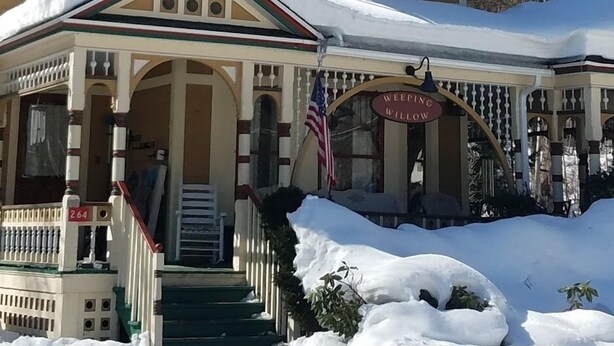 Un edificio de dos pisos con tejado cubierto de nieve y un porche con un letrero que dice 'Weeping Willow'.