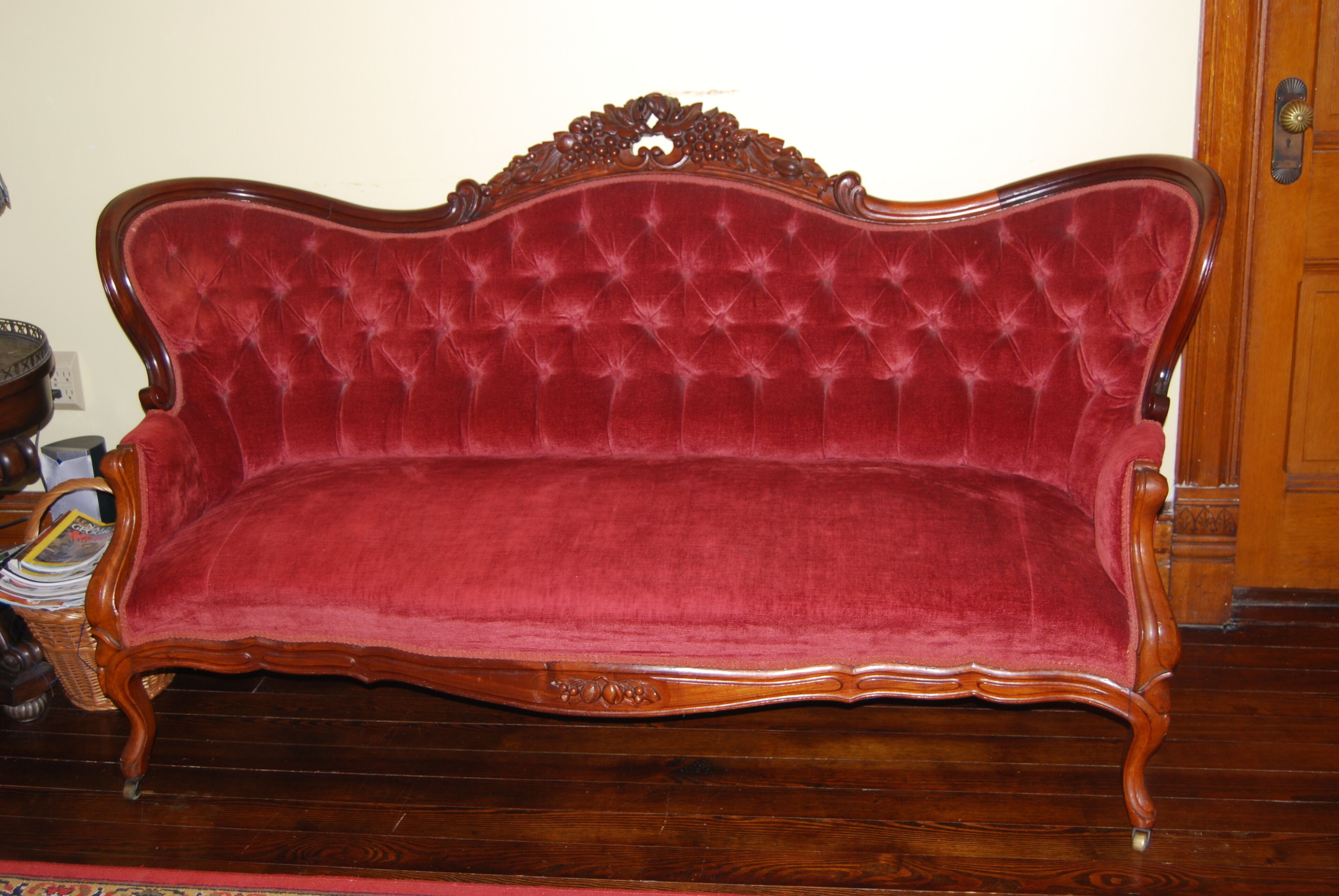 A red velvet sofa with a wooden frame and ornate carvings.