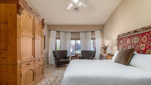 A bedroom with a large bed, a wooden wardrobe, two armchairs, a small table, and a window with curtains.