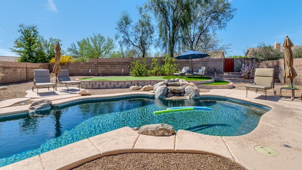 A backyard with a swimming pool, lounge chairs, and a patio area.