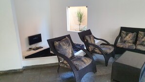 Un salon avec deux fauteuils en osier, un petit téléviseur posé sur un meuble et un ventilateur de plafond.