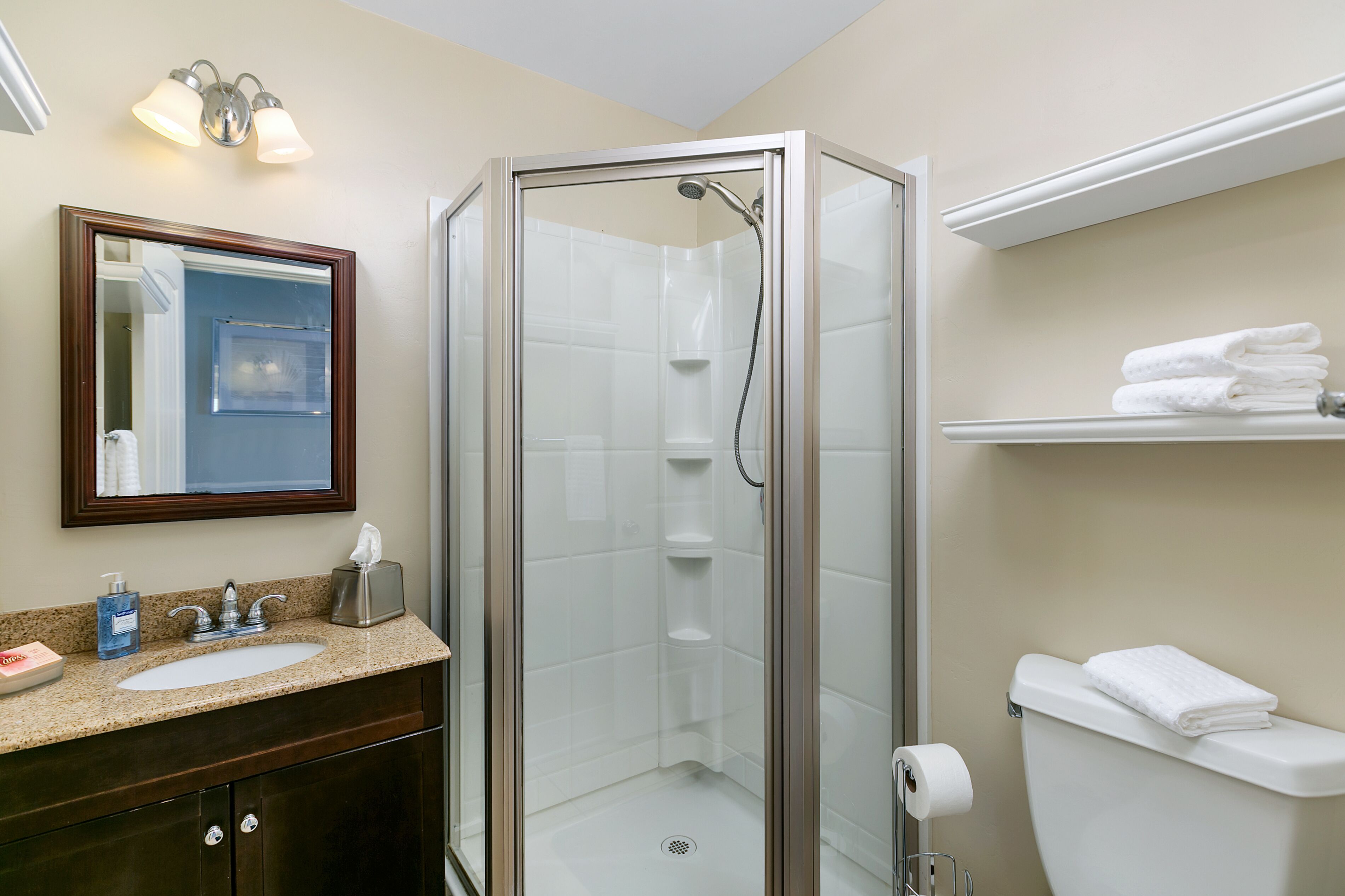 Une salle de bain avec une douche à parois de verre, un lavabo avec un miroir au-dessus et des toilettes sur lesquelles est posée une serviette.