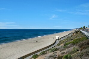 A coastal road with a beach on the right, a lifeguard tower, and a clear blue sky. - Carlsbad Cottage by the Beach (Carlsbad)