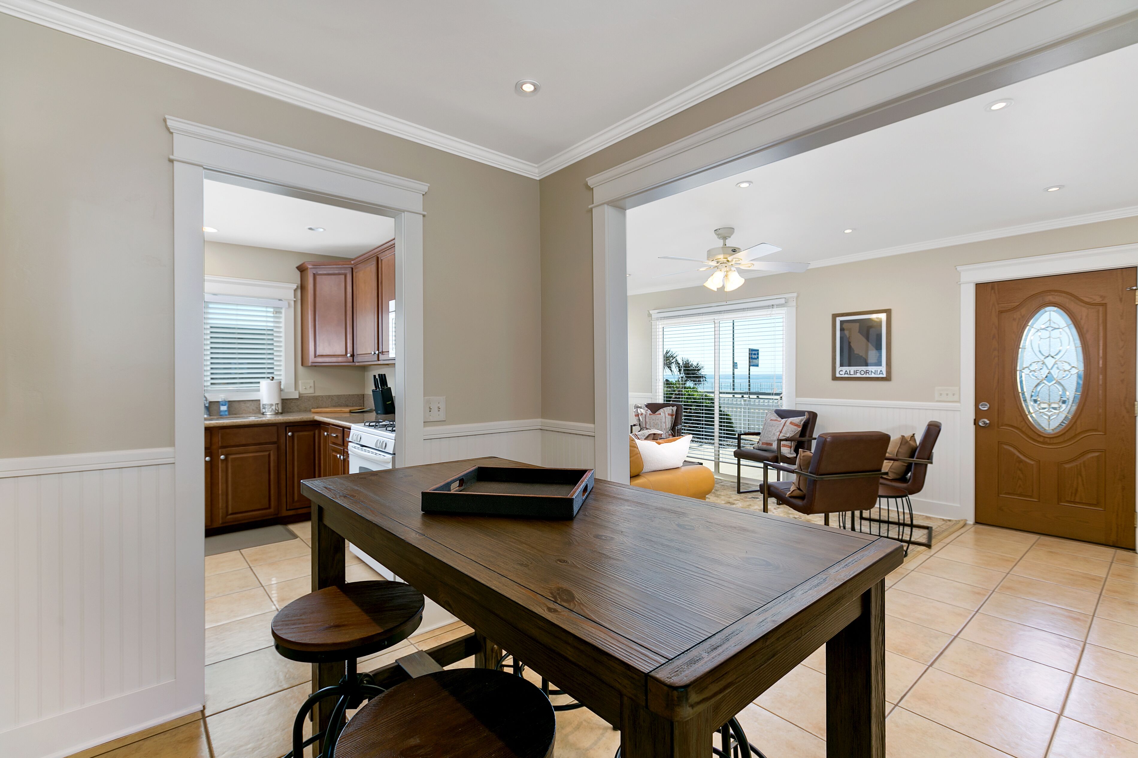 Un comedor amplio con mesa y sillas de madera, una cocina al fondo y una puerta que da a un balcón con vistas.