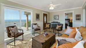 A spacious living room with a view of the ocean, a ceiling fan, and a cozy seating area with a coffee table. - Carlsbad Cottage by the Beach (Carlsbad)