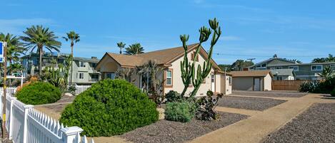 A residential area with houses, a white picket fence, and various plants.