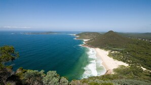 A coastal landscape with a beach, ocean, and forested hills. - Barefoot, 7/44 Marine Drive - Fabulous Fingal Bay (Fingal Bay)